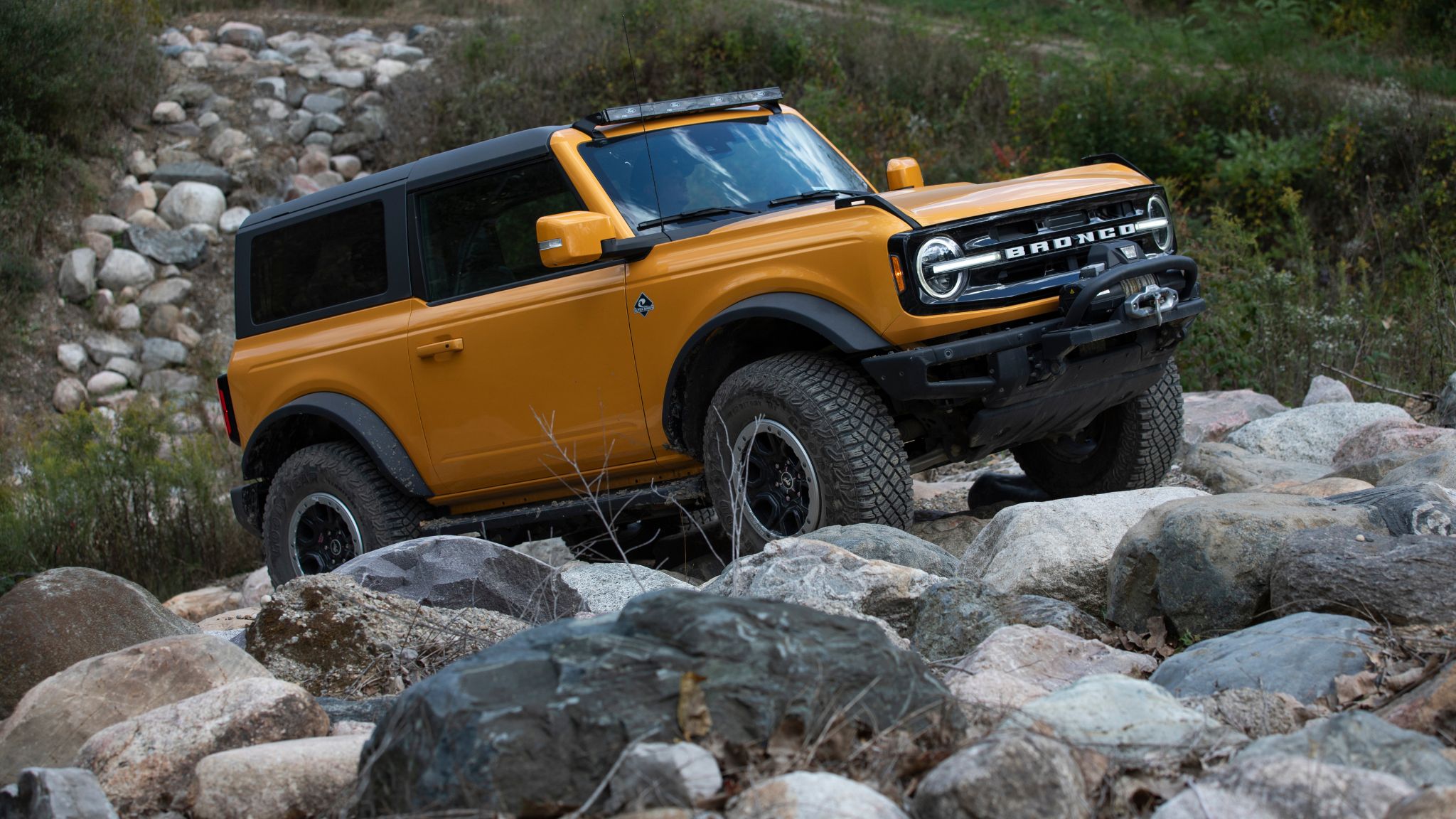 An orange Ford Bronco crawls over rocks at an incline.
