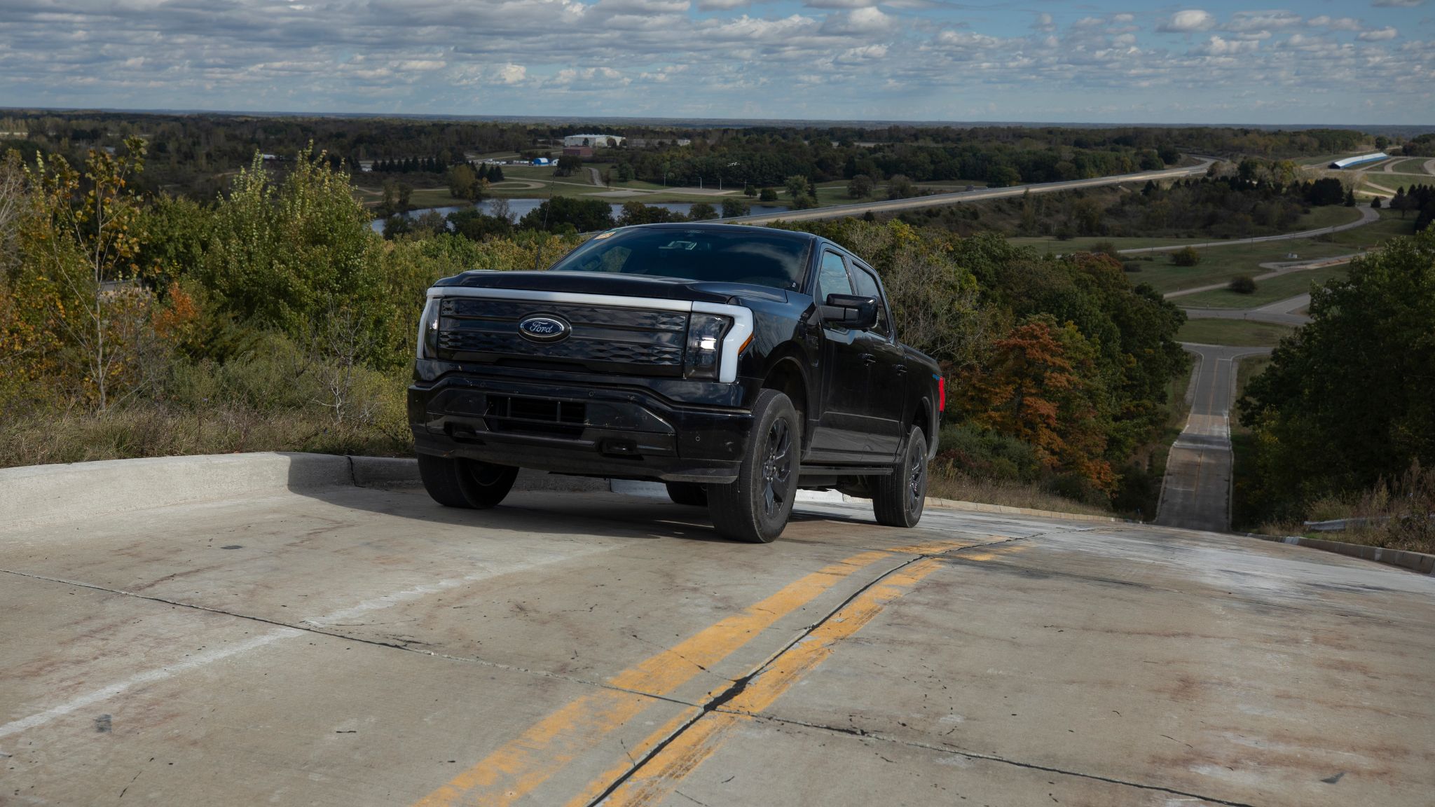 A black Ford truck drives up a very steep incline on a road.