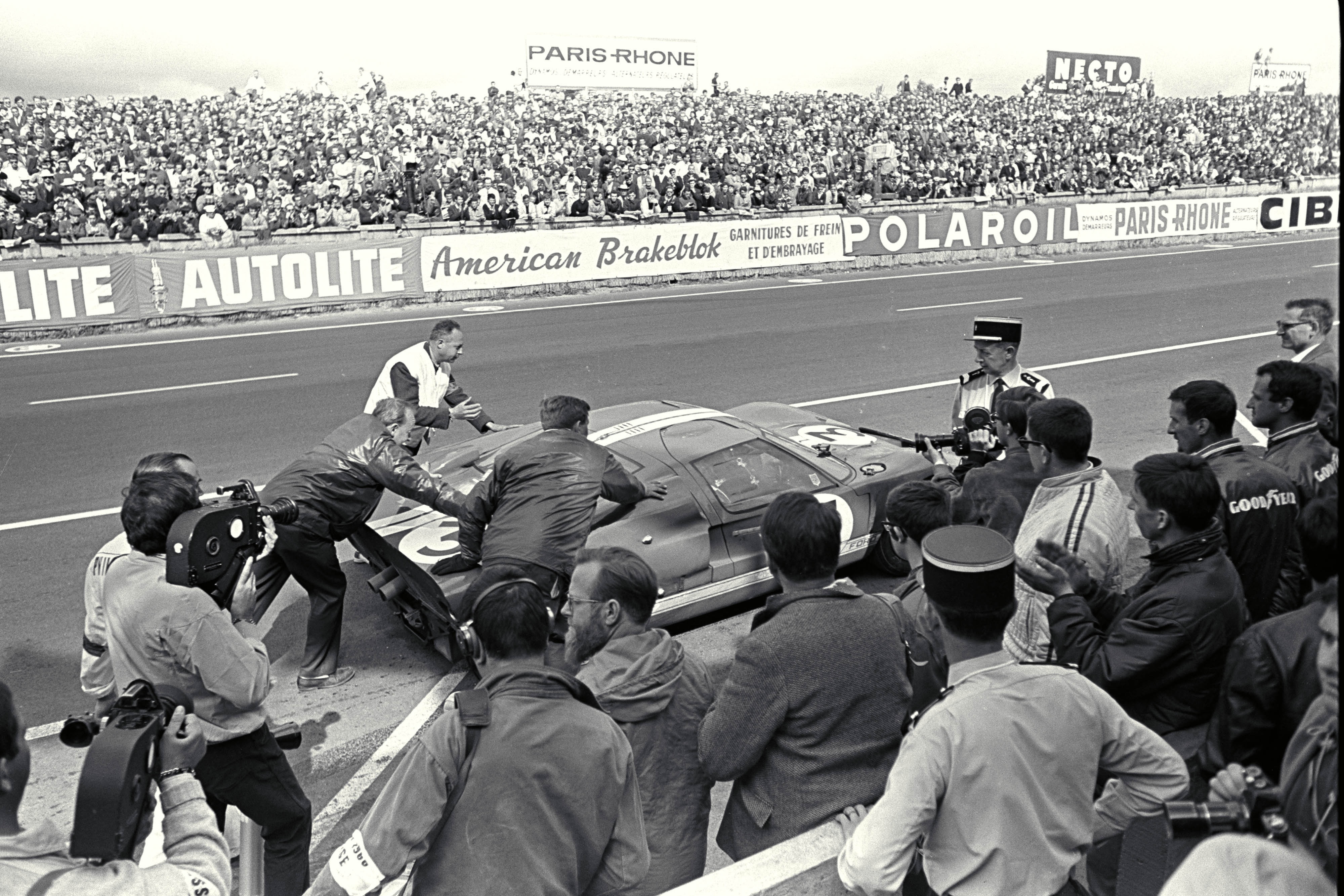 A black and white photo of a pit stop on a racetrack in 1966.