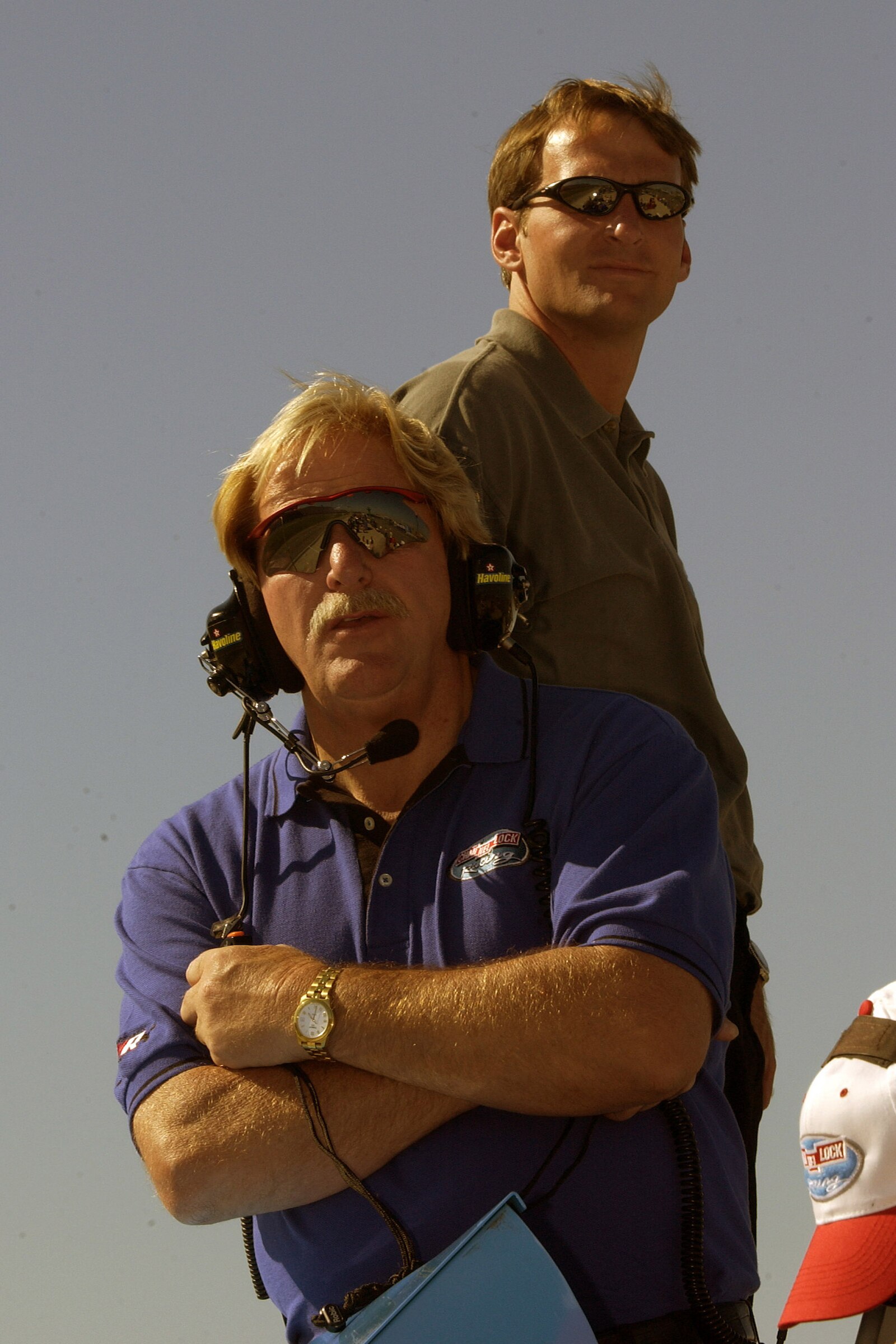 Two men wearing sunglasses pose for a photo at a NASCAR event.