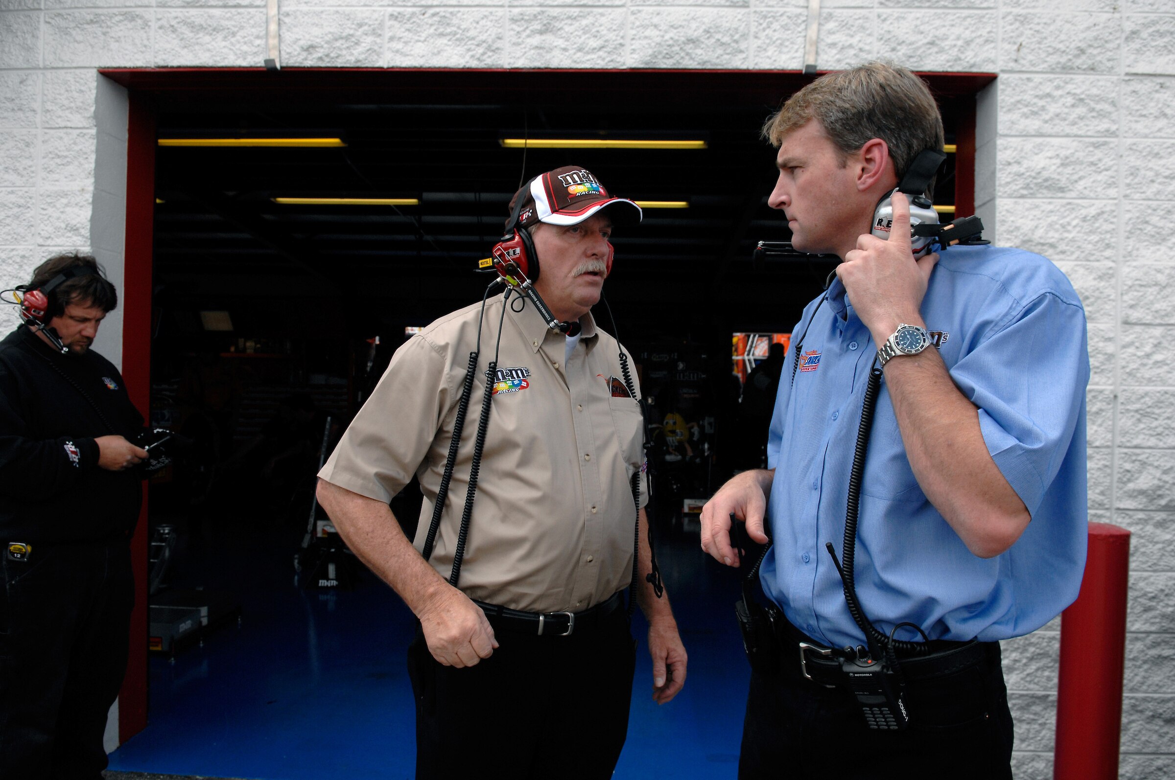 Two men wearing headphones speak at a NASCAR event.