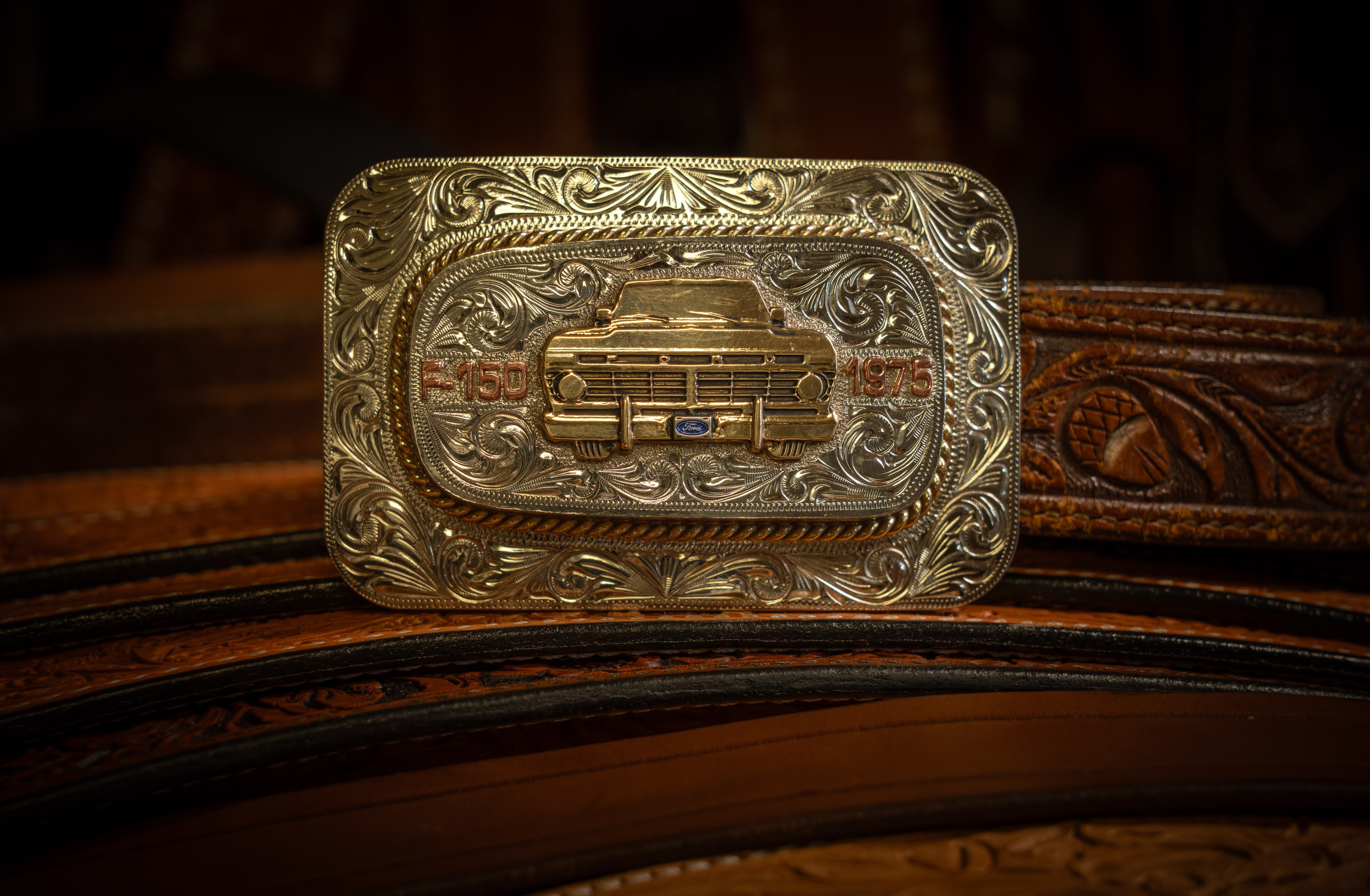 The front of an ornate gold belt buckle with a truck on it.