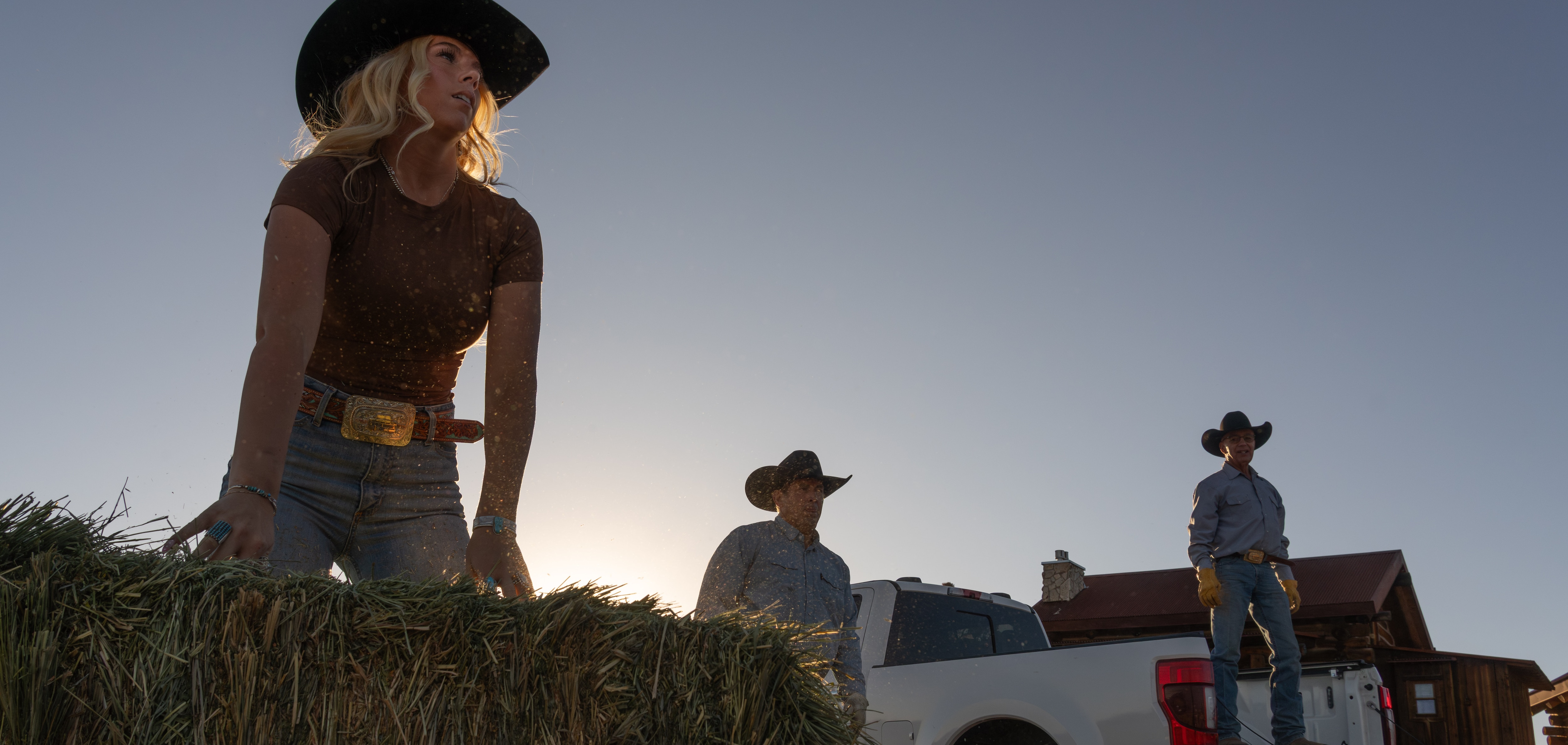 A young woman wearing a cowboy hat lifts a bale of hay.